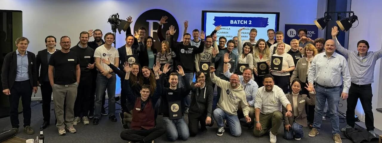 Group photo of the Batch 2 participants at Reaktor Wildau, many with raised hands, with a screen reading “Batch 2” in the background